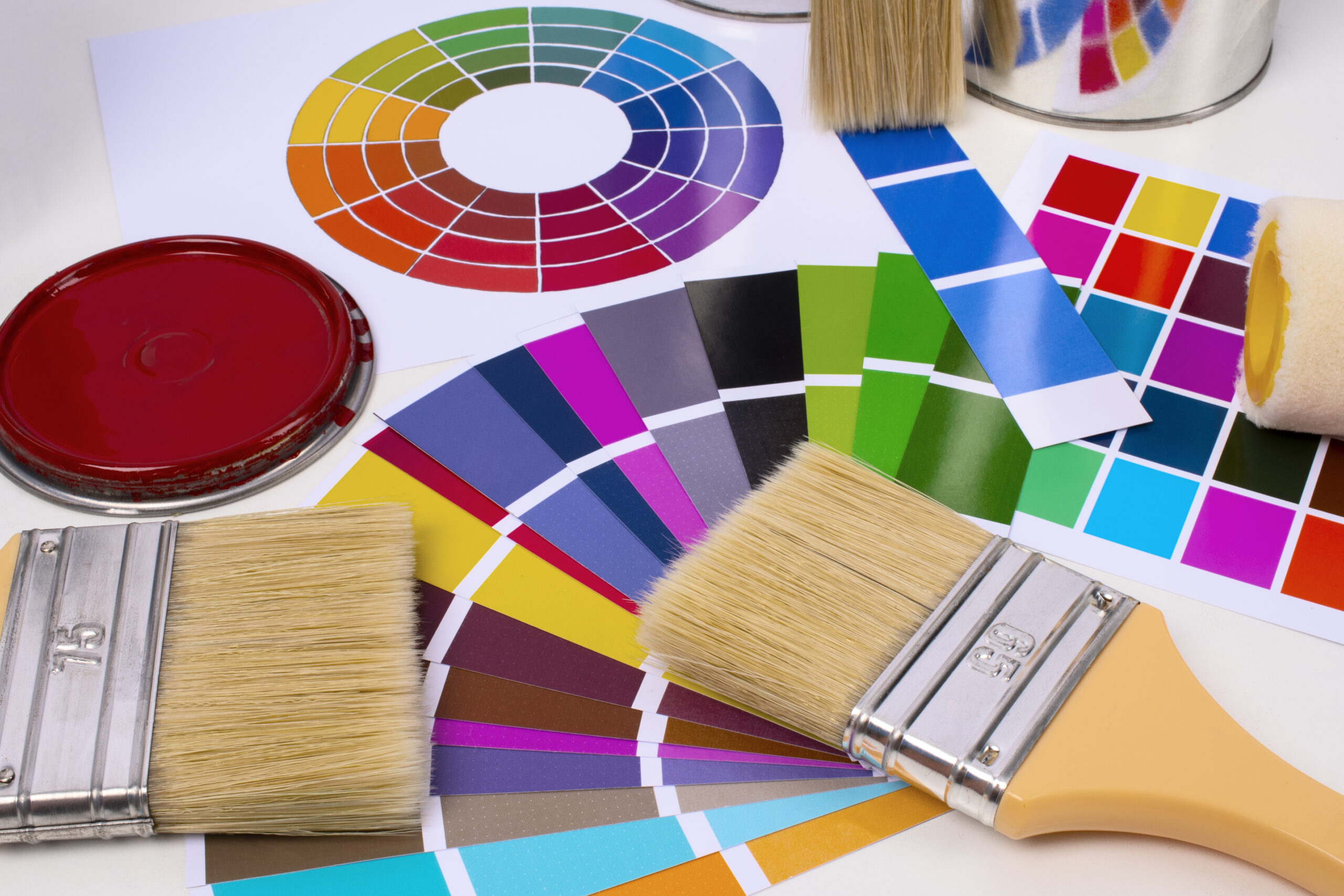 Home renovation painting tools, including brushes and a roller, resting on a color wheel and vibrant paint swatches.
