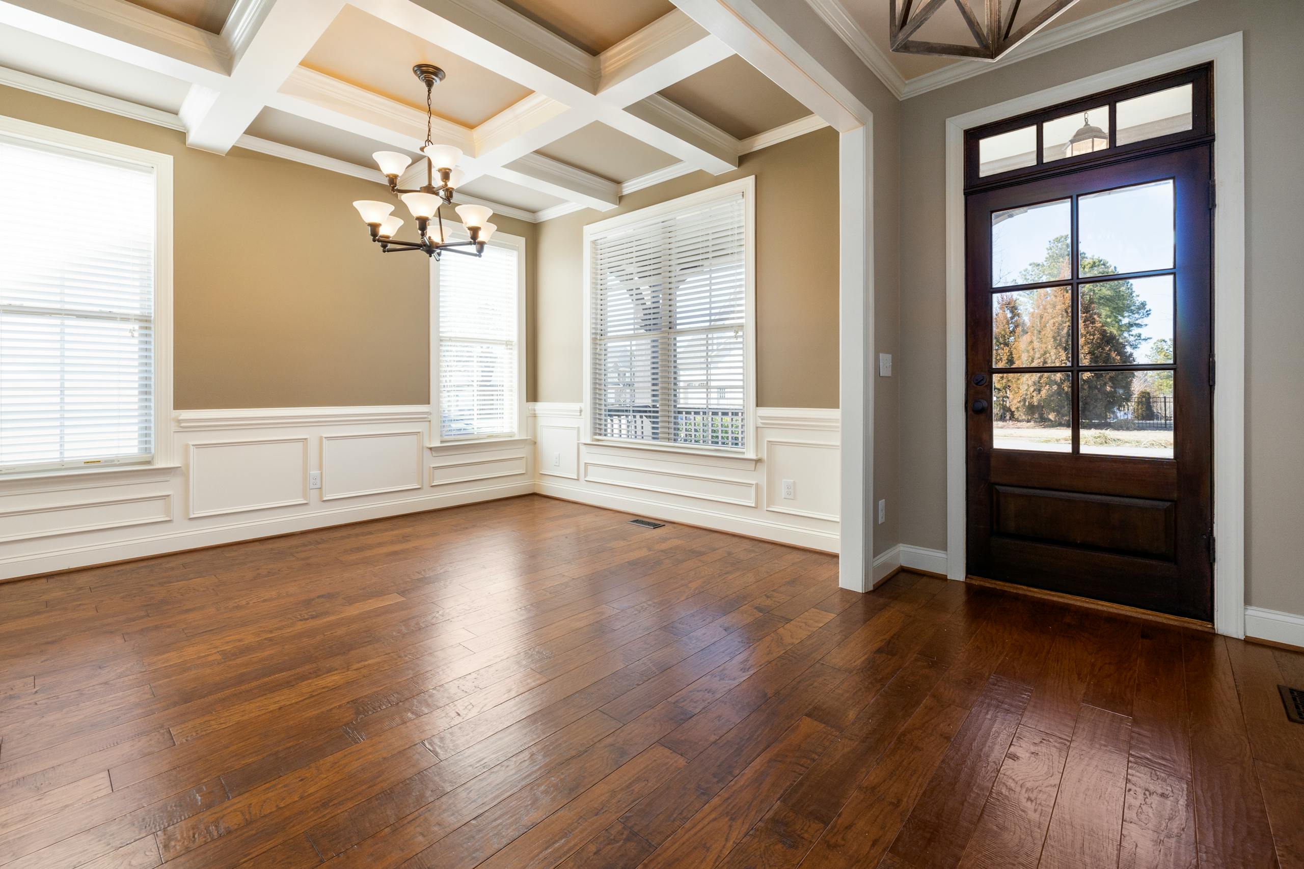 Spacious empty living room with wooden flooring, large windows, and ceiling lights.